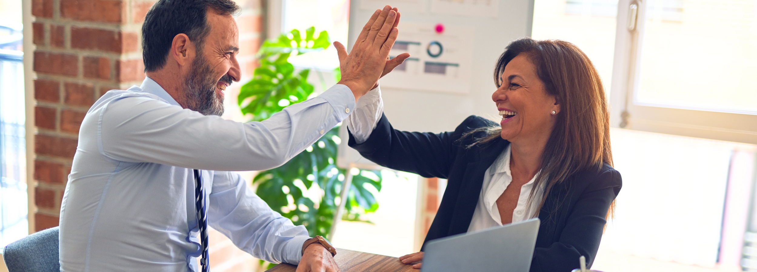Ein bärtiger Mann und eine Frau im Blazer feiern einen Erfolg mit einem High-Five im Büro.

Das Bild zeigt zwei Personen, einen Mann und eine Frau, die sich an einem Schreibtisch befinden und sich gegenseitig ein High-Five geben. Beide scheinen sich zu freuen, vermutlich über einen geschäftlichen Erfolg. Der Mann trägt ein hellblaues Hemd mit Krawatte und hat einen gepflegten Bart. Die Frau trägt eine weiße Bluse unter einem schwarzen Blazer. Vor ihnen steht ein Laptop auf einem hölzernen Schreibtisch. Im Hintergrund ist eine Ziegelwand, eine Pflanze und eine Tafel mit Diagrammen und Notizen zu sehen. Die Atmosphäre ist positiv und energiegeladen, was durch das Lachen und die Mimik der beiden Personen verstärkt wird. Die Stimmung ist harmonisch und vermittelt den Eindruck eines gut funktionierenden Teams.