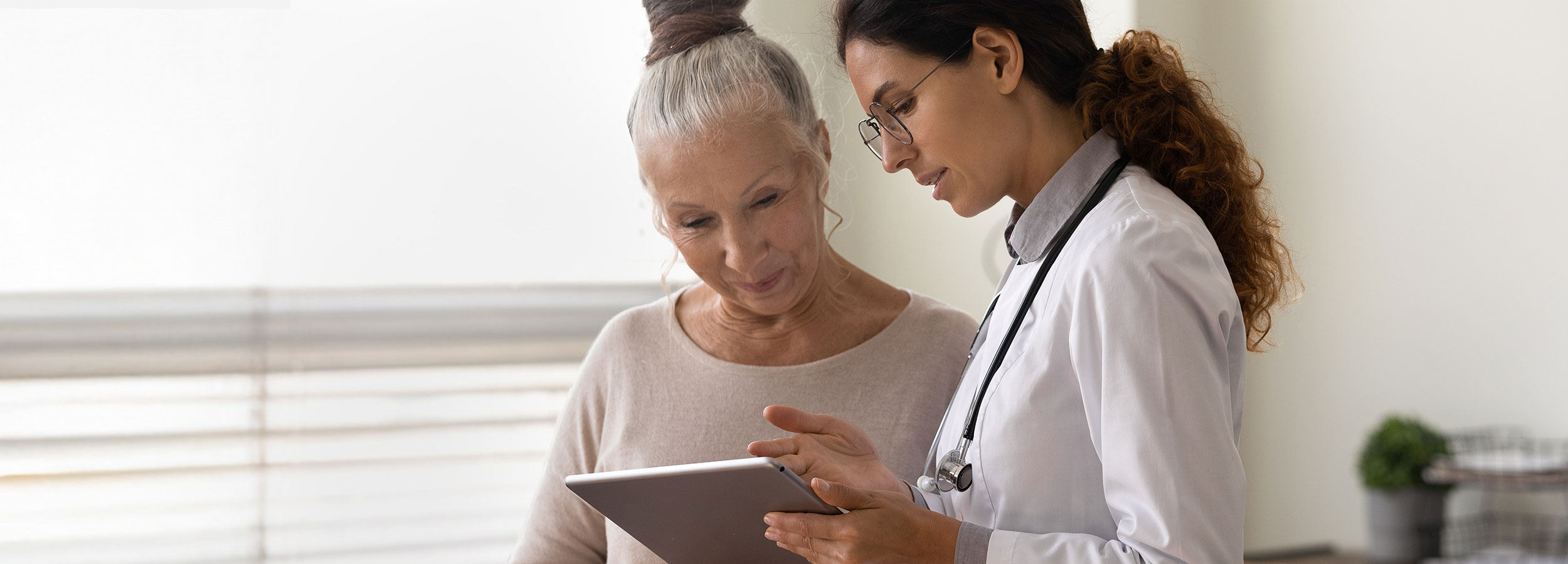 Eine ernsthafte Ärztin zeigt einer älteren Patientin den Bildschirm eines Tablets